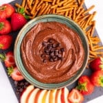 a bowl of dark chocolate hummus surrounded with fresh fruit and pretzels