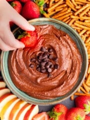 a strawberry being dipped into dark chocolate hummus