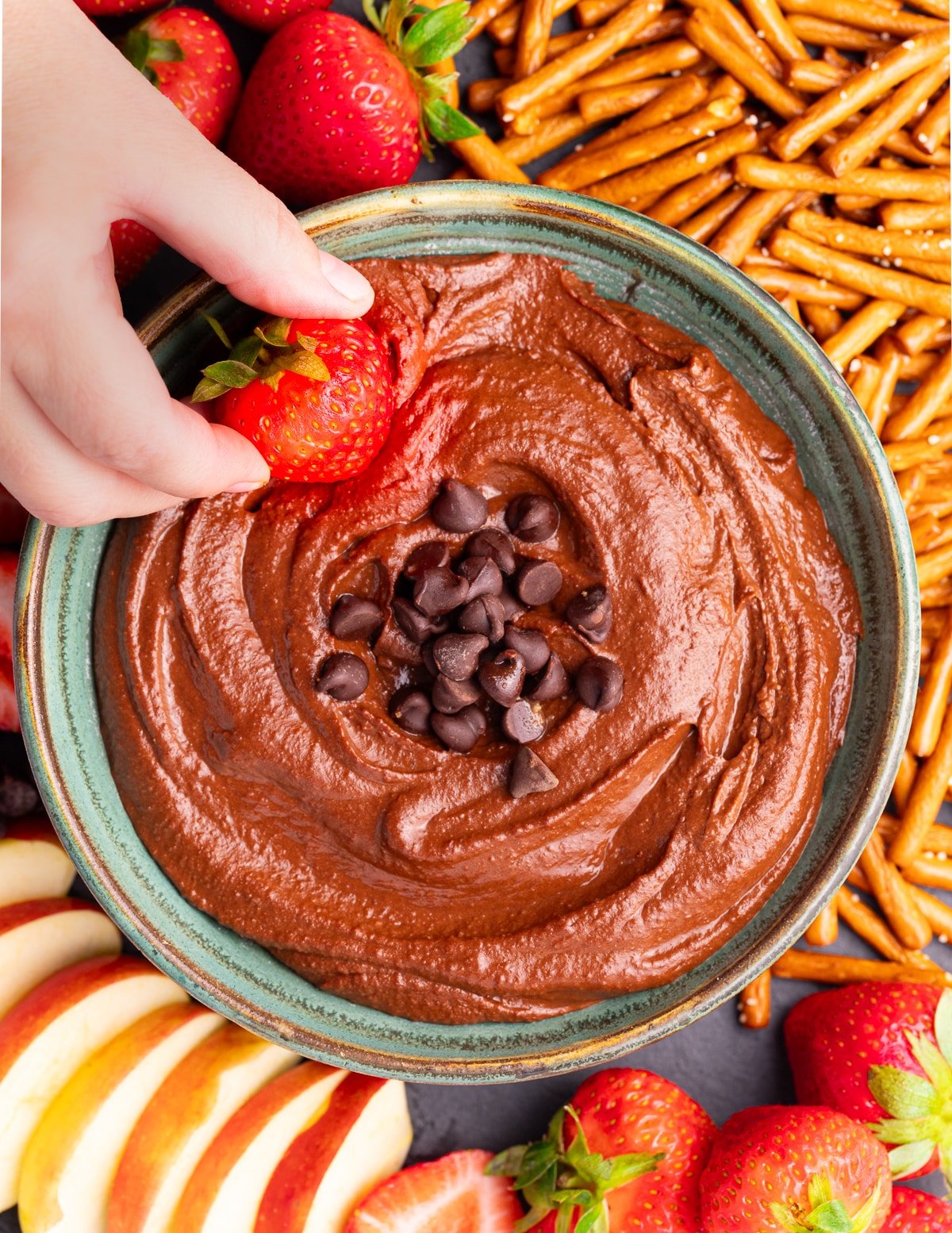 a strawberry being dipped into dark chocolate hummus