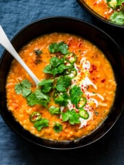 a bowl of curry lentil soup topped with cilantro leaves, vegan yogurt, and sliced jalapeno