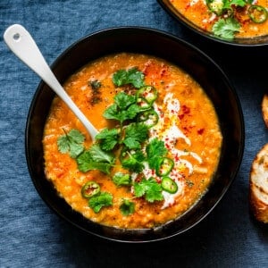 a bowl of curry lentil soup topped with cilantro leaves, vegan yogurt, and sliced jalapeno