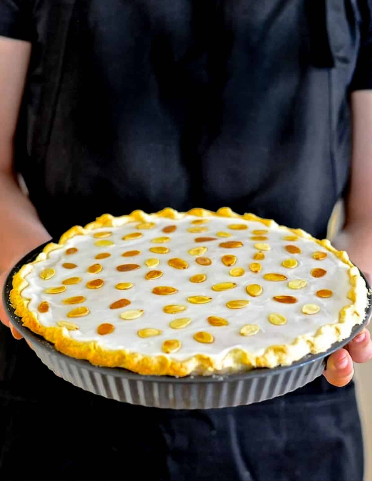 a person in a black apron holding an iced mincemeat tart.