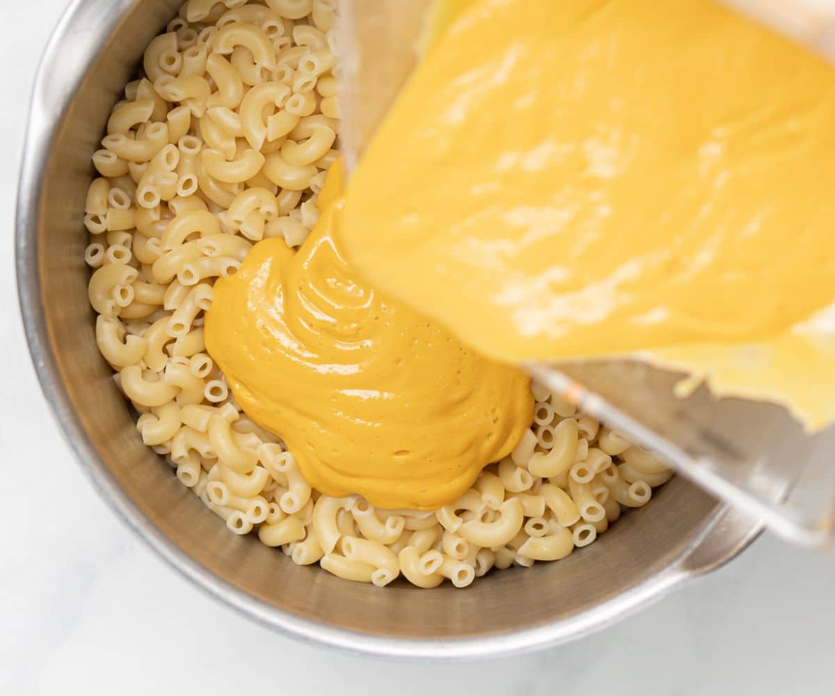 vegan cheese sauce pouring into a pan of cooked macaroni