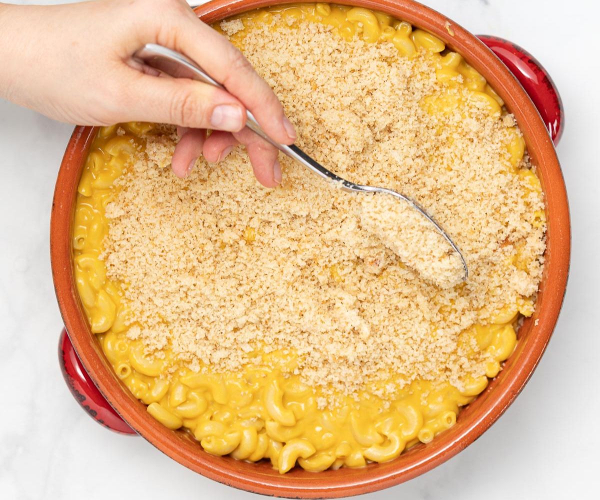 a spoon sprinkling breadcrumbs on a dish of mac and cheese