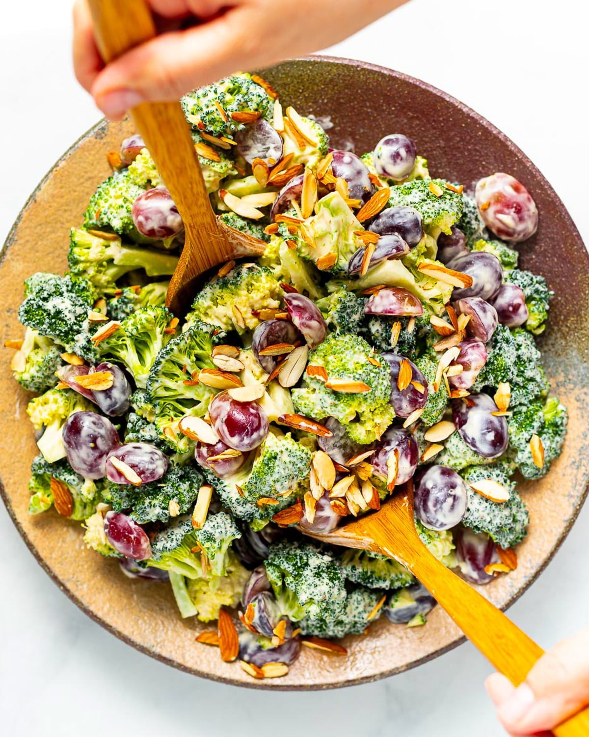 a salad bowl of vegan broccoli salad with wooden salad servers inside