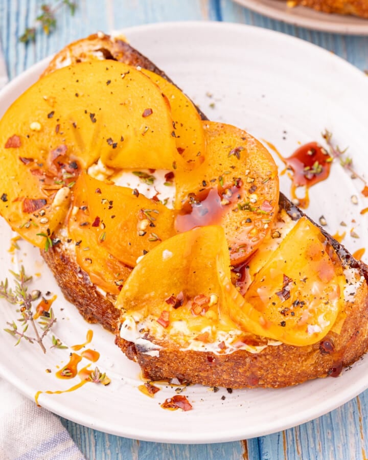 a piece of toast with persimmon, cream cheese, vegan honey, chili, thyme, salt and pepper.