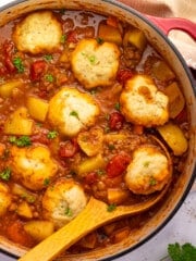 a pan of vegan beef & baked bean stew with a dumpling resting on a wooden spoon