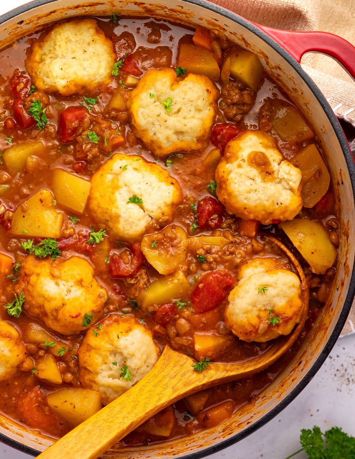a pan of vegan beef & baked bean stew with a dumpling resting on a wooden ladle