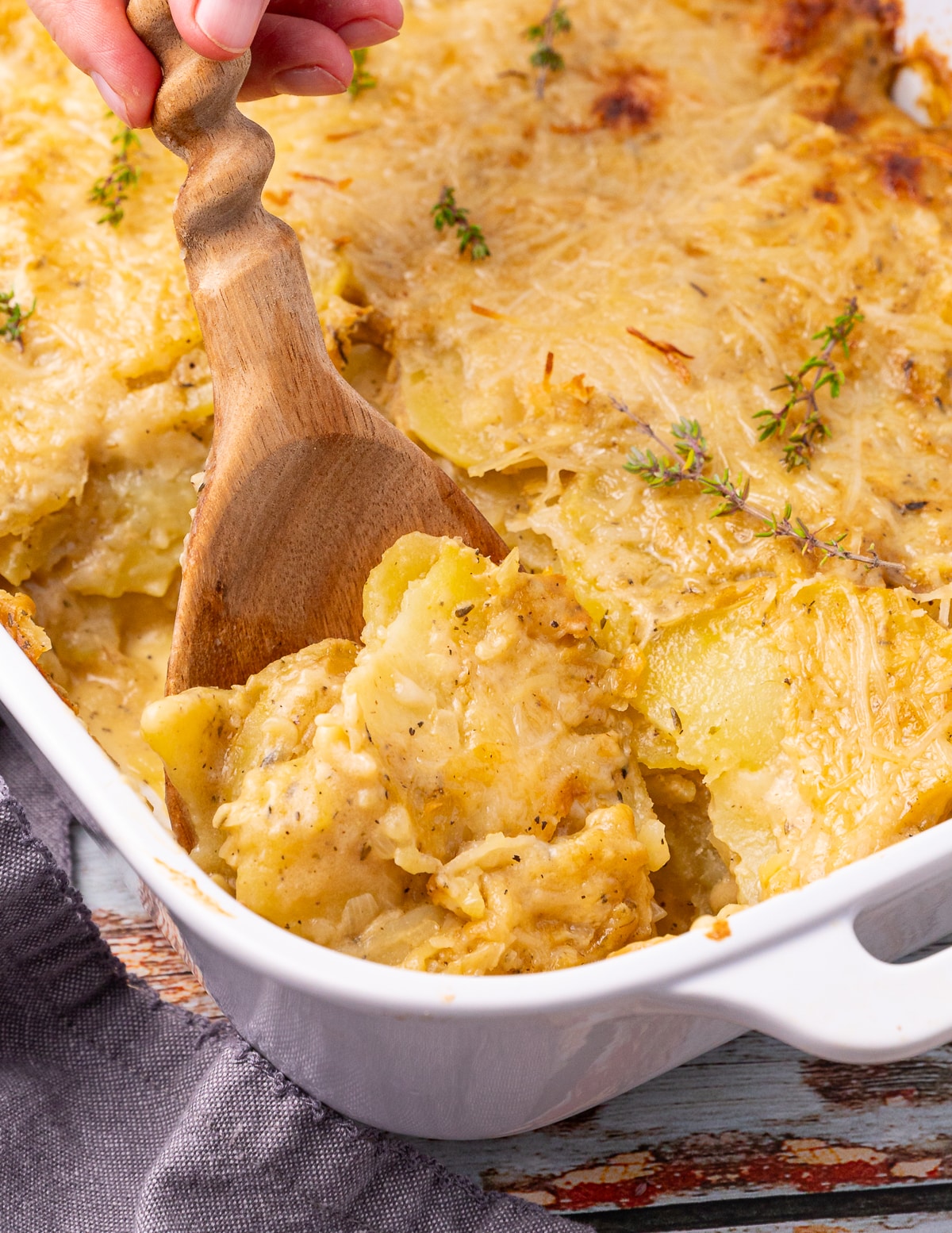 a wooden spoon digging into cheesy, saucy, scalloped potatoes