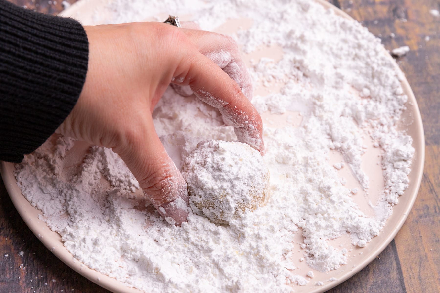 a snowball cookie being rolled in powdered sugar