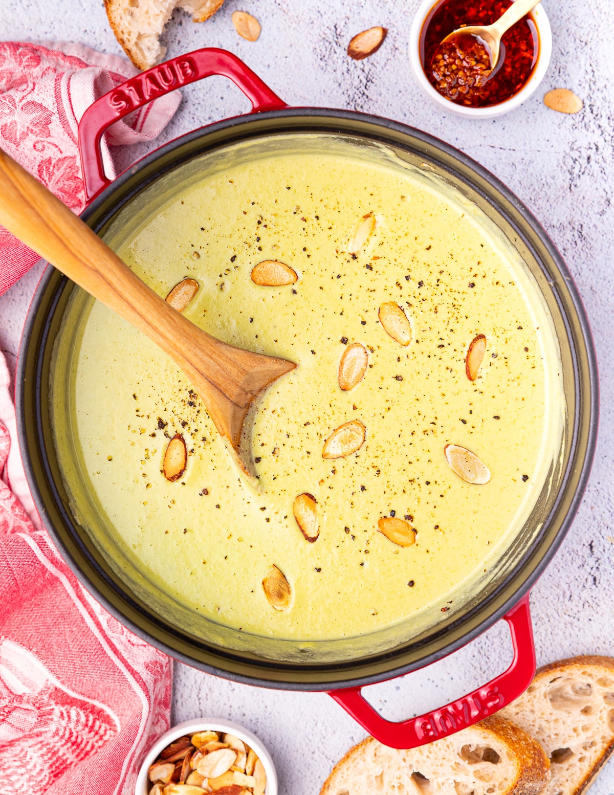 creamy broccoli almond soup in a staub pan with black pepper and toasted flaked almond garnish