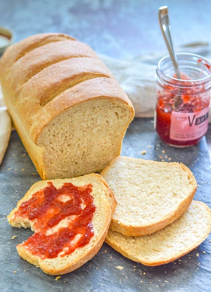 a partially sliced loaf of bread with jam on one piece