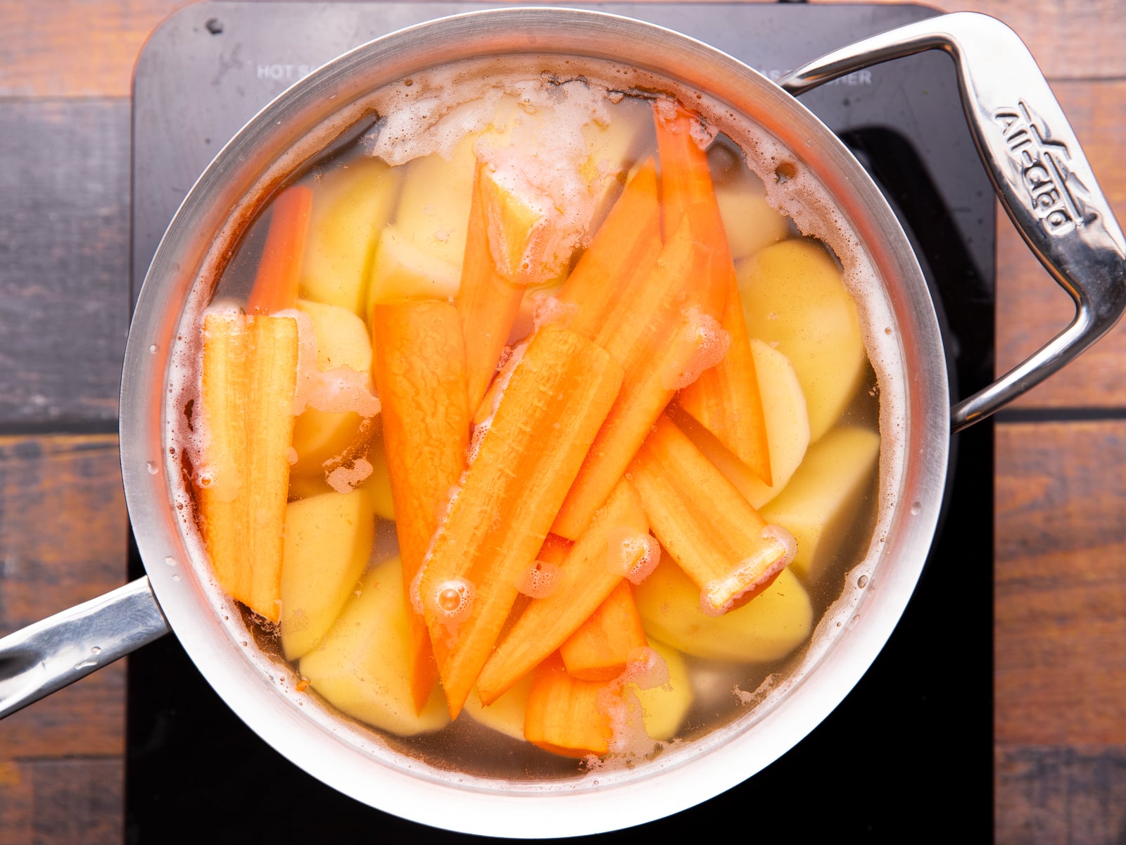 a pan with parboiling potatoes and carrots