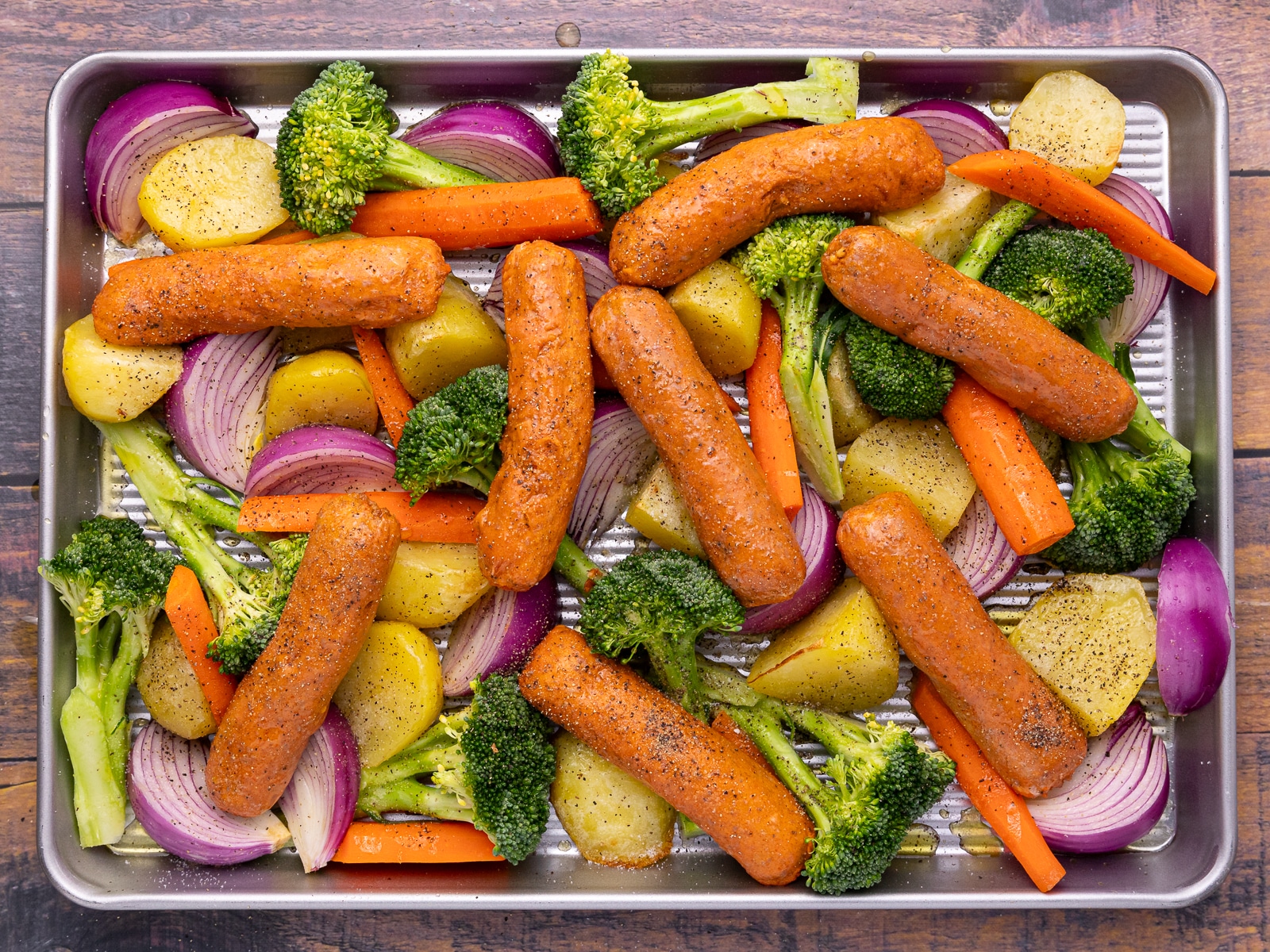 uncooked sausages and vegetables on a baking tray