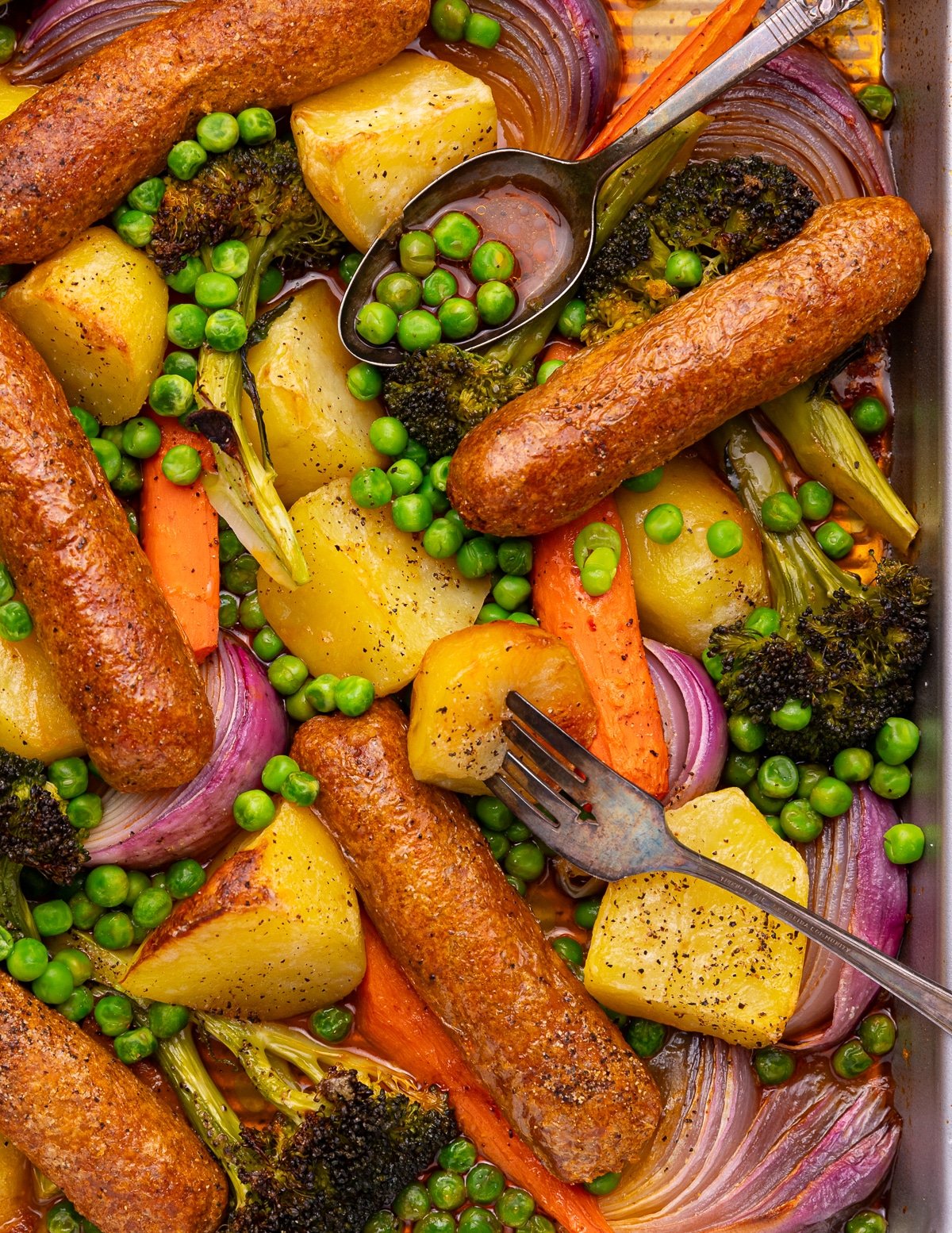a vegan sheet pan sausage dinner with a fork and spoon.