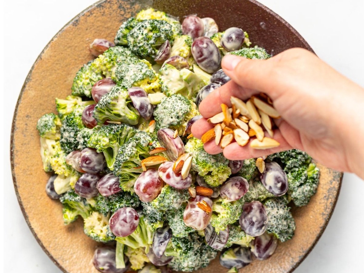 a hand sprinkling slivered almonds over the broccoli salad