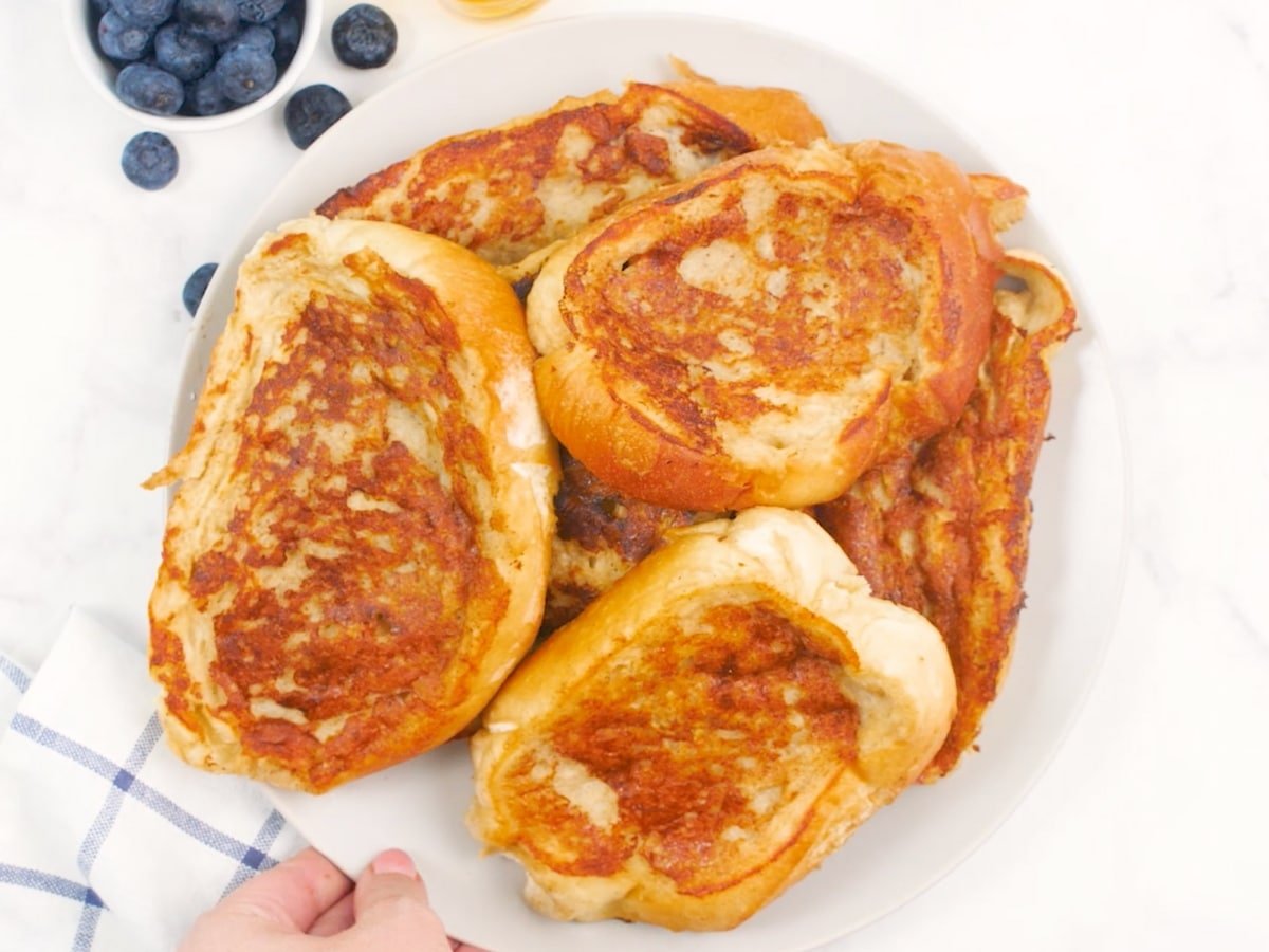 a big pile of Vegan French Toast on a plate next to a bowl of blueberries.