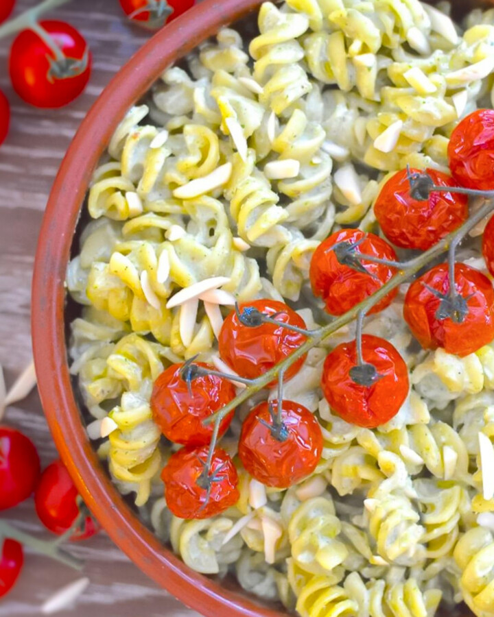a bowl of creamy vegan pesto pasta topped with cherry tomatoes