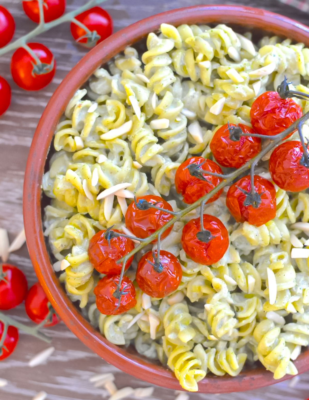 a terracotta bowl of creamy pesto pasta topped with roasted cherry tomatoes on the vine.
