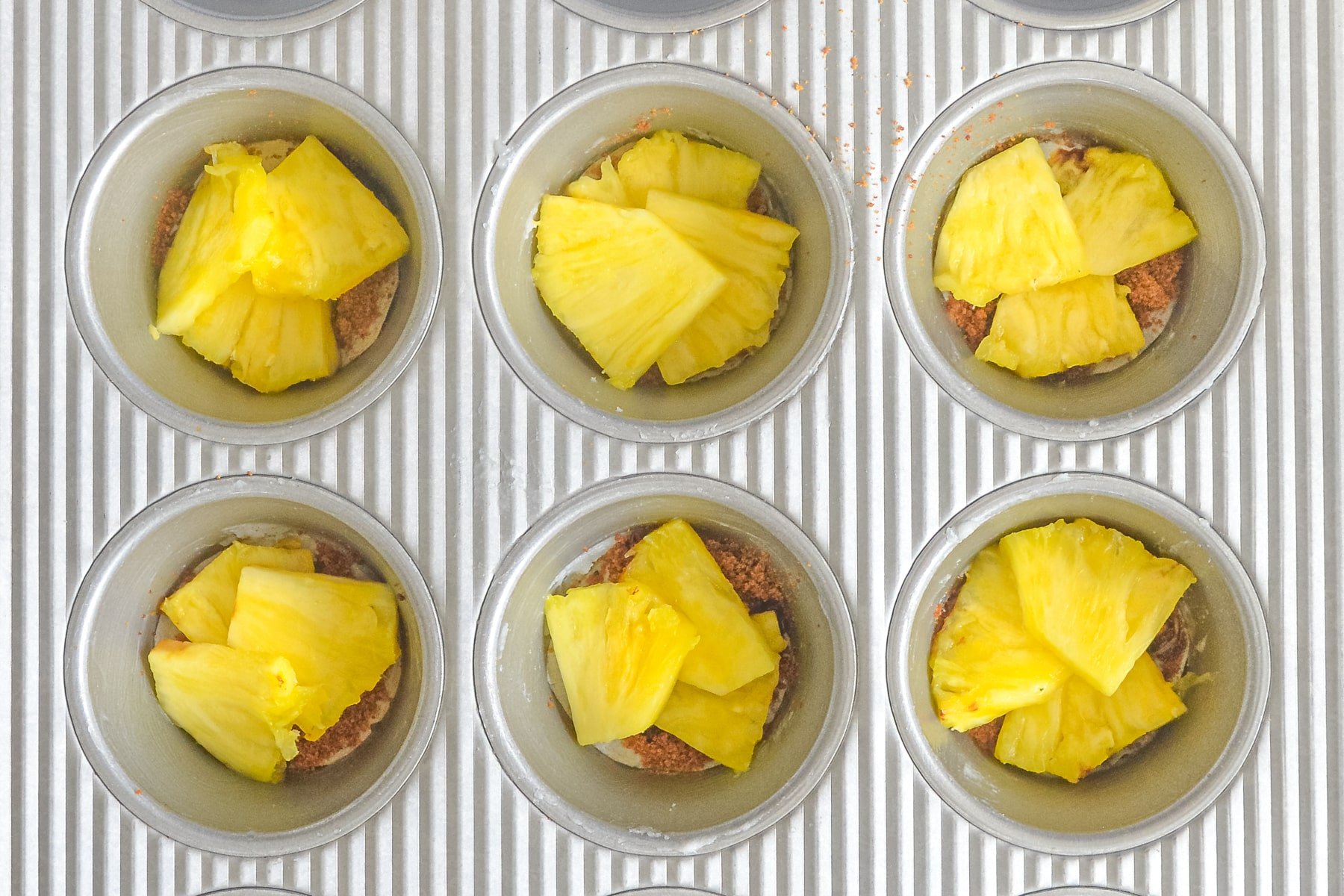 a muffin pan with brown sugar and pineapple in the bottom of the wells. 