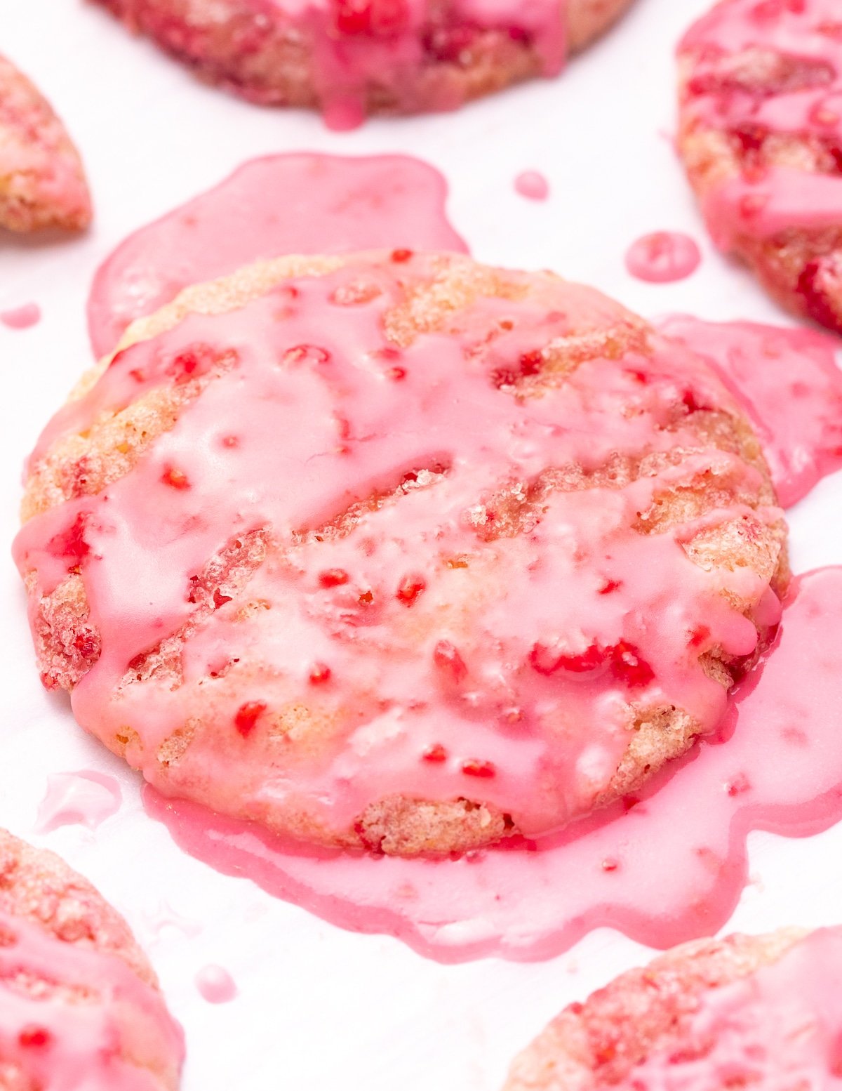 one vegan raspberry cookie drizzled in lots of drippy raspberry glaze. Puddles of it surround the cookie. 