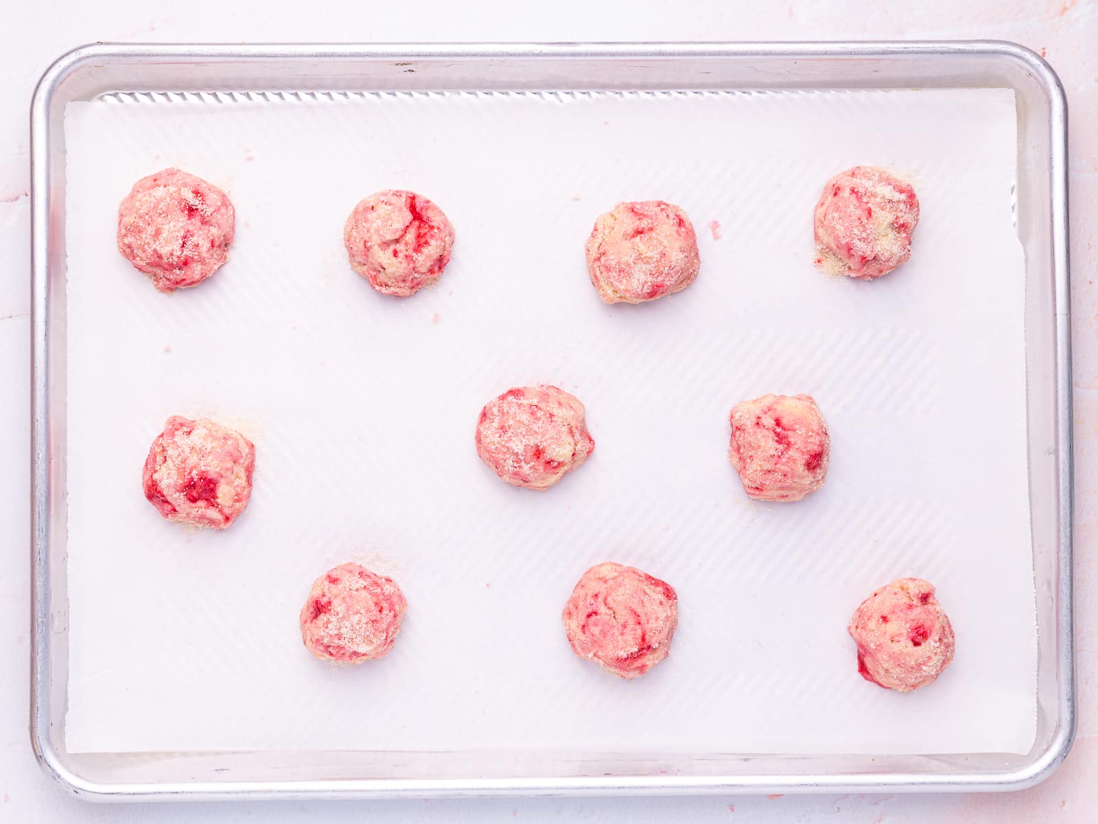 balls of raspberry cookie dough on a parchment paper lined baking tray