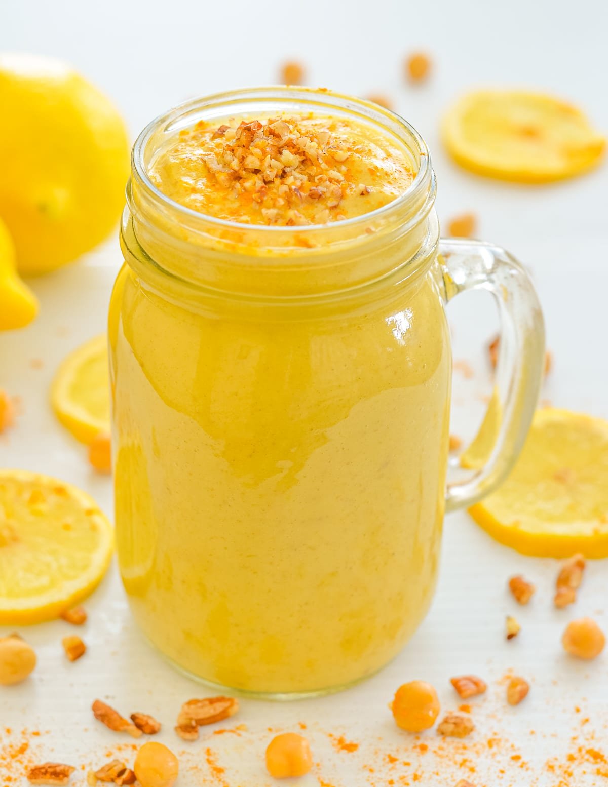 a glass of lemon cheesecake smoothie surrounded by a scattering of chickpeas and lemon slices.