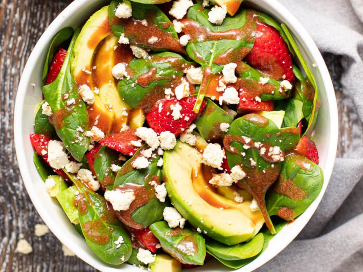 strawberry spinach salad wirh drizzles of strawberry vinaigrette and a scattering of vegan feta