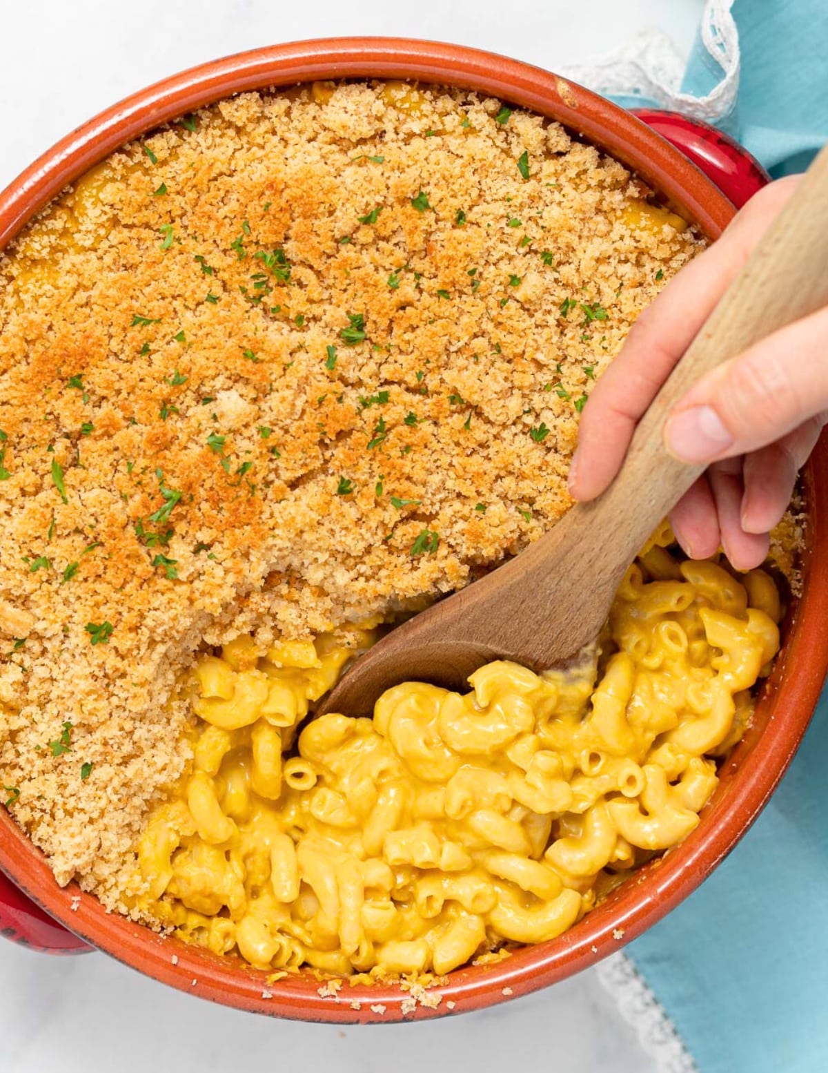 a spoon scooping out some baked macaroni and cheese from a terracotta baking dish