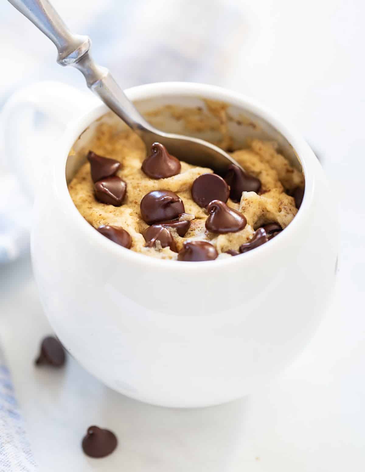 a chocolate chip cookie in a mug with a spoon in it
