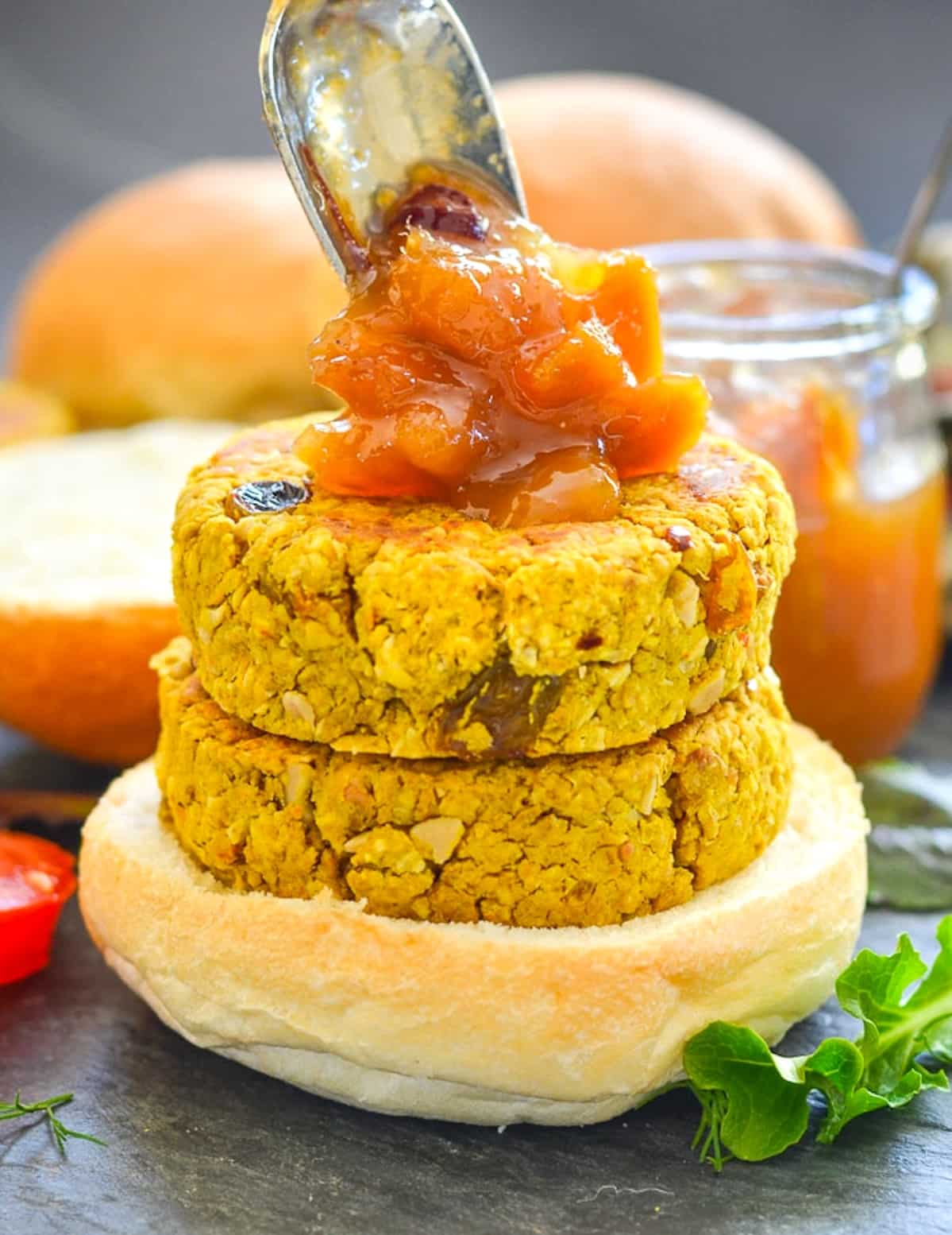 2 stacked curried chickpea burgers on a bun with a dollop of mango chutney/