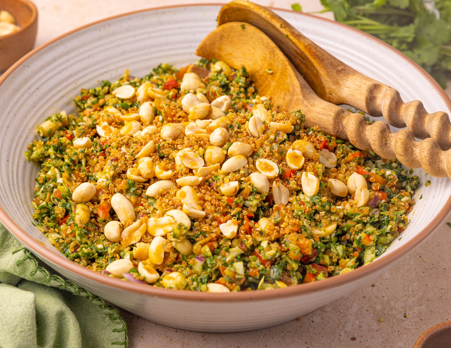 Crispy quinoa kale salad in a white bowl with wooden salad servers. 