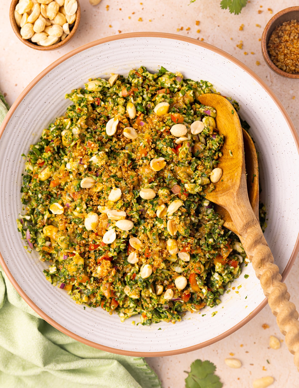 A white bowl full of crispy quinoa kale salad, with wooden salad servers tucked in the side and a green napkin. 