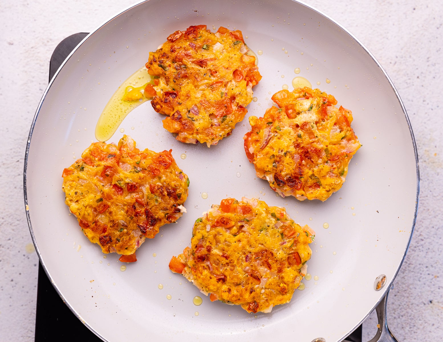 golden tomato fritters in a frying pan. 