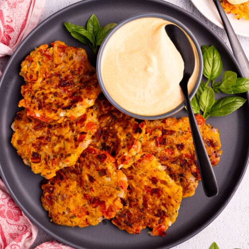 tomato fritters on a black plate with a bowl or sriracha mayo and fresh basil.