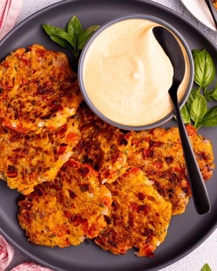 tomato fritters on a black plate with a bowl or sriracha mayo and fresh basil.