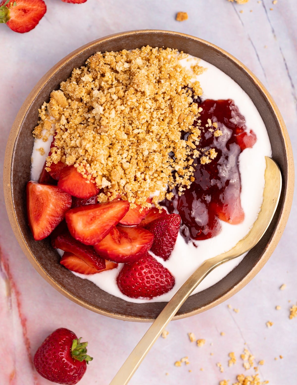 a bowl of dairy-free natural yogurt topped with strawberry jam, strawberries, and buttery cookie crumbs. 