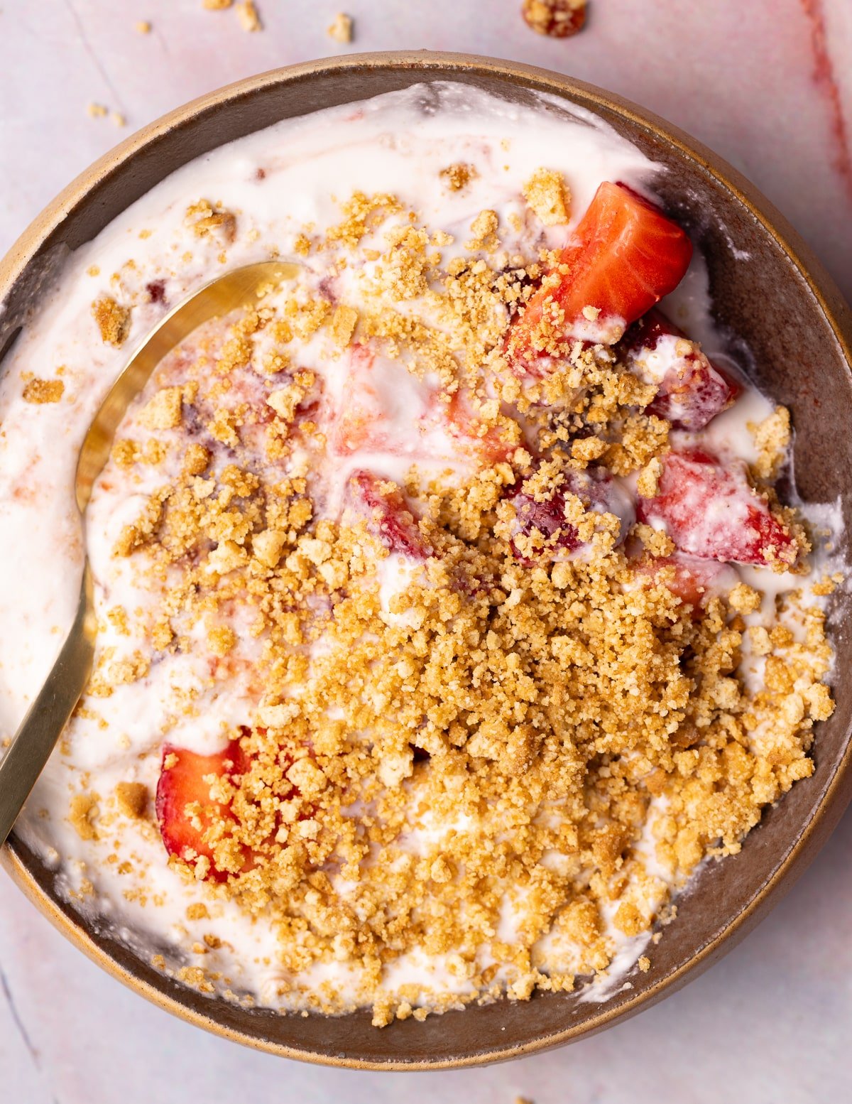 a bowl of yogurt with strawberries, strawberry jam, and cookie crumbs.