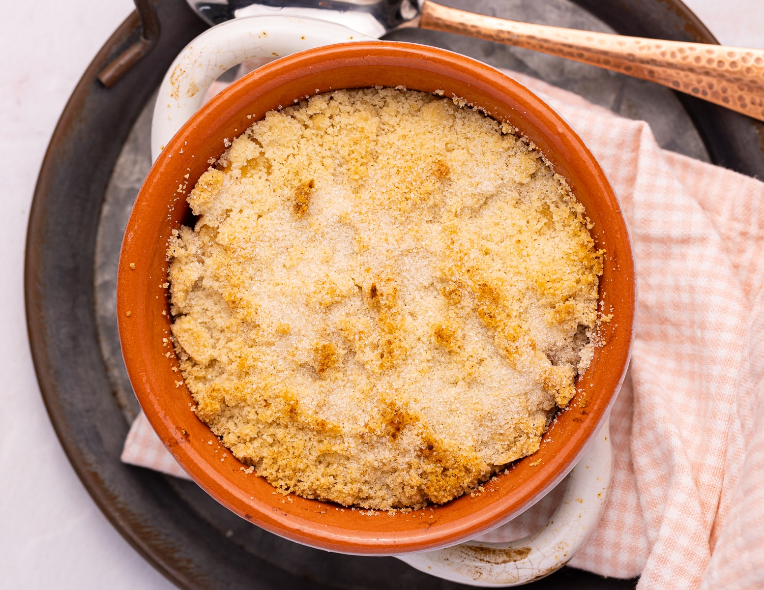 golden cooked peach crumble in an oven proof dish with a pink and white checked napkin.