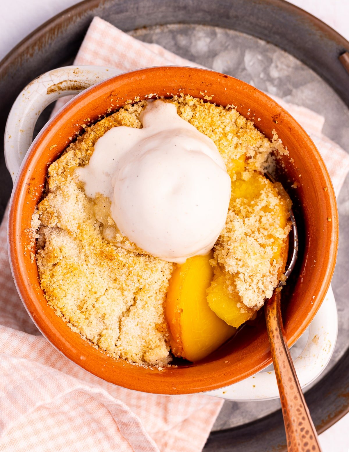 a single-serve peach crumble in a dish with a dollop if ice cream