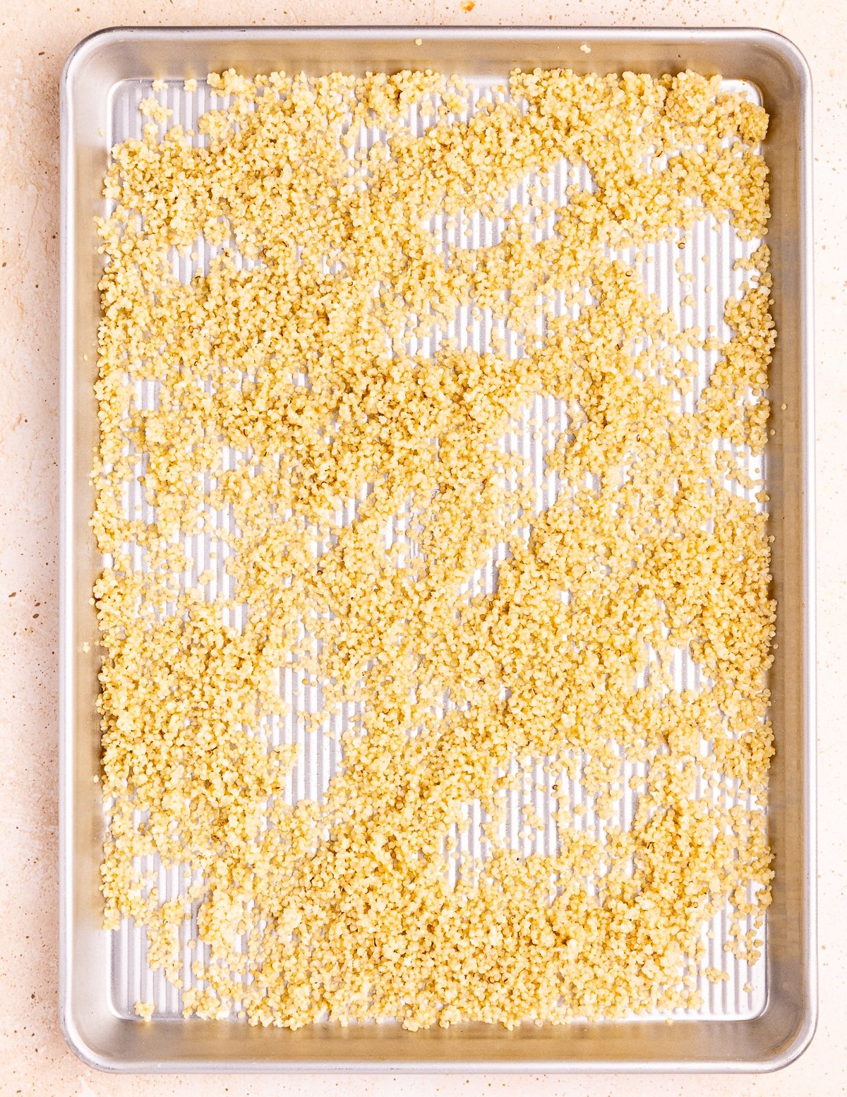 a baking tray with cooked quinoa spread in a thin layer on it. 