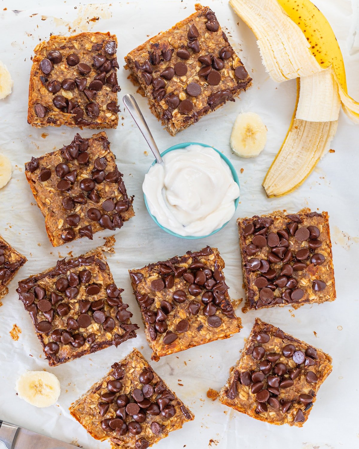 chocolate peanut butter banana oatmeal bars with a bowl of yogurt and a peeled banana. 