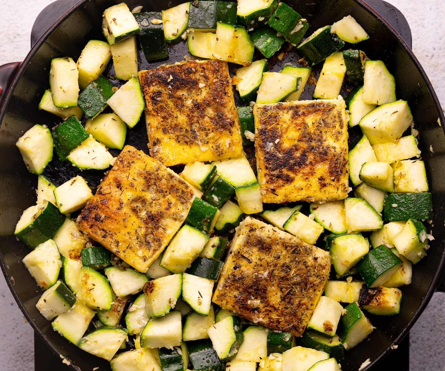 golden, herby, tofu squares and cubed zucchini in a skillet.