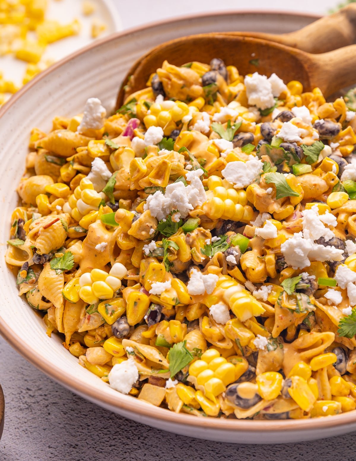 close up photo of a large bowl of vegan Elote Pasta Salad with a scattering of vegan feta cheese. 