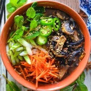 a bowl of udon noodle soup with fresh veggies and herbs.