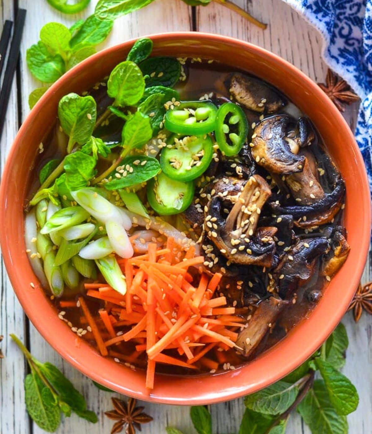 a bowl of udon noodle soup topped with shredded carrots, herbs, and mushrooms.