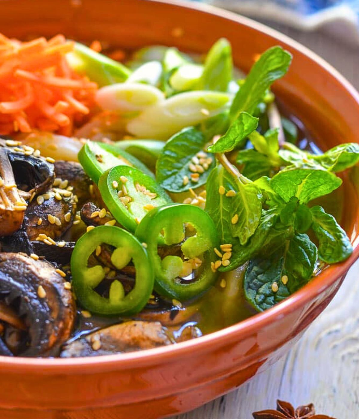 herbs and jalapenos on a bowl of udon noodle soup