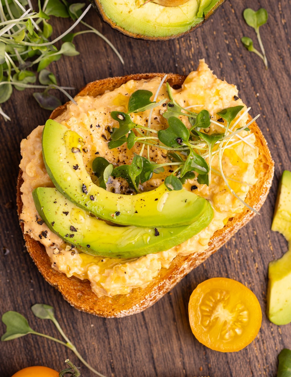 a piece of toast topped with sliced avocado, sprouts, freshly ground black pepper and a drizzle of extra virgin olive oil. 