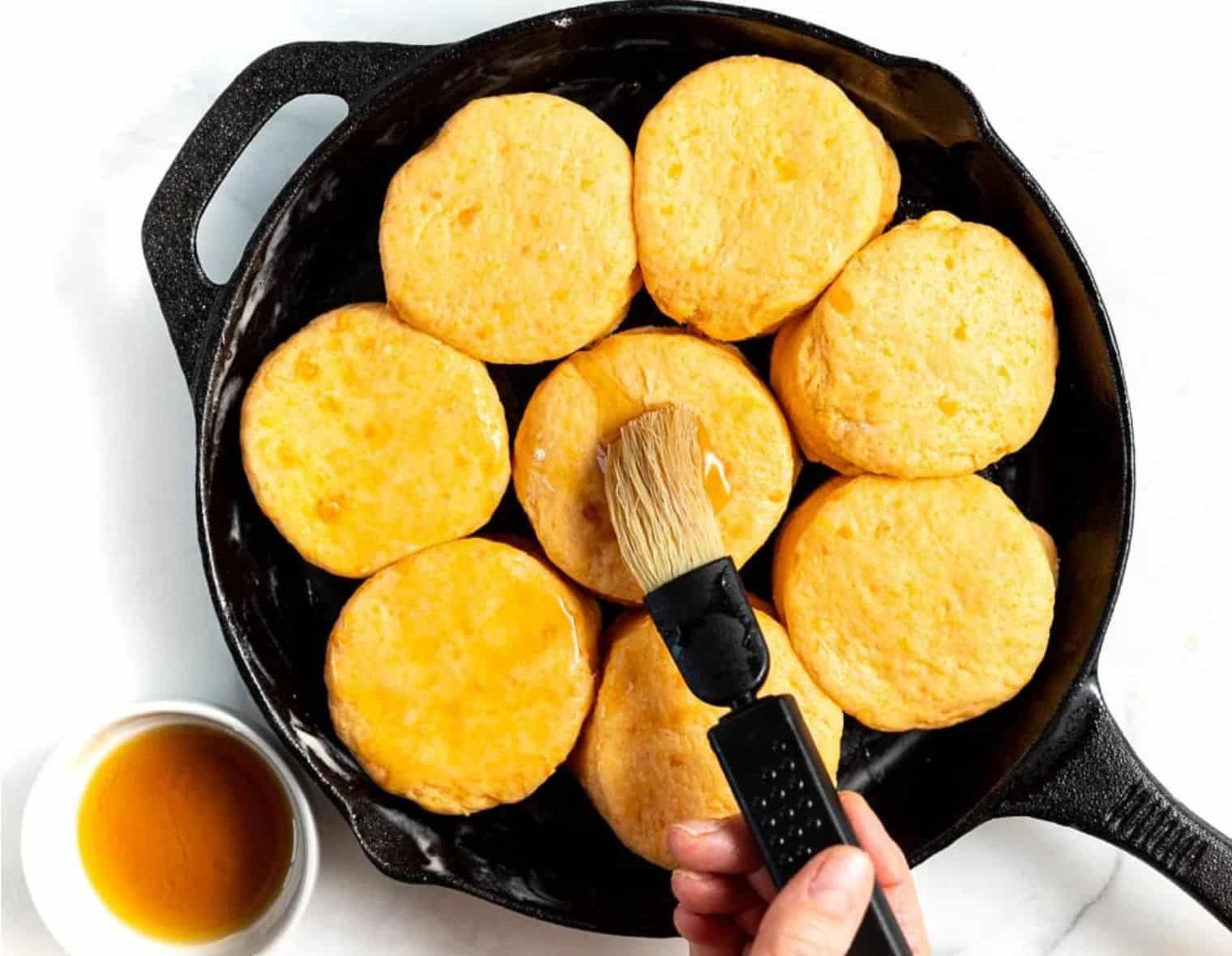 uncooked sweet potato biscuits in a skillet being brushed with maple syrup. 