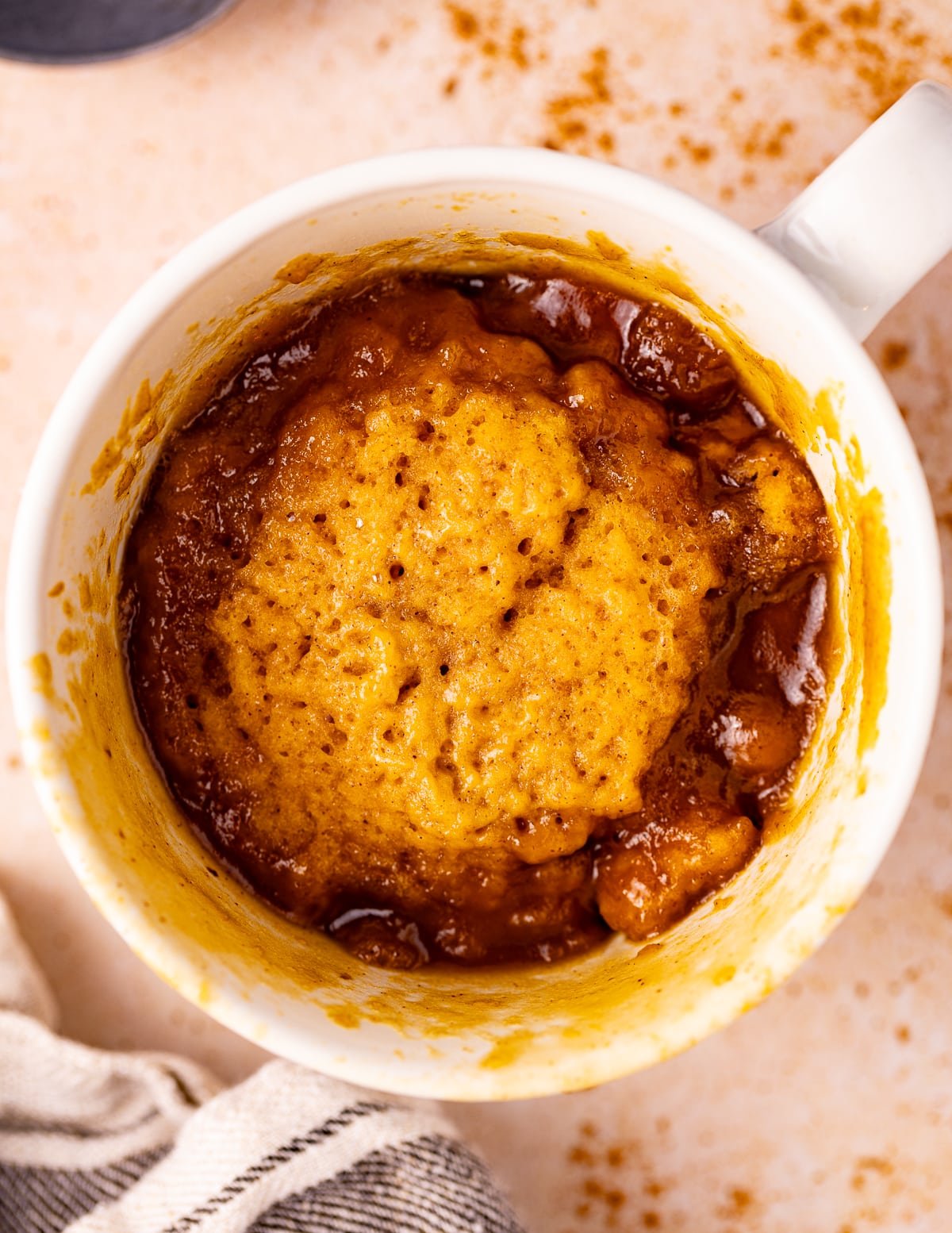 A gorgeous orangey colored fluffy pumpkin mug cake in a mug with lots of crusty bubbly caramel sauce around the edges. 